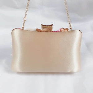 Detail of champagne satin evening clutch with 3D floral accents and diamond clasp