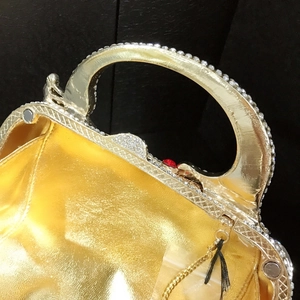 Détail d'une pochette de soirée avec poignée en strass et cadre en métal doré texturé
