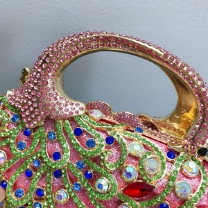 Détail d'une pochette phénix diamantée montrant des strass roses et une poignée dorée