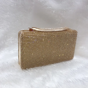 Dettaglio pochette da sera dorata con strass scintillanti e manico superiore ondulato