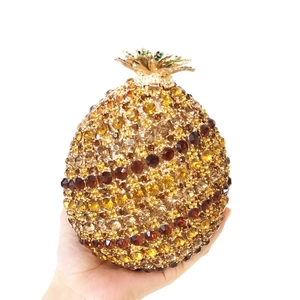 Detail of crystal-encrusted pineapple clutch bag with golden leaf clasp and amber rhinestones