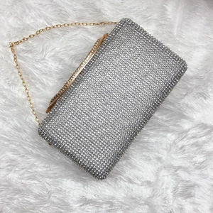 Dettaglio pochette da sera con strass argento e catena oro su sfondo di peluche bianco