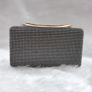 Dettaglio della pochette da sera nera rettangolare con strass e manico in metallo oro