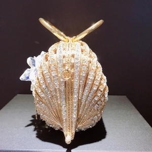 Détail d'une pochette de soirée en forme de coquillage doré avec strass et anse papillon