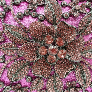 Detail of pink rhinestone flower and glitter finish on a luxury evening clutch bag