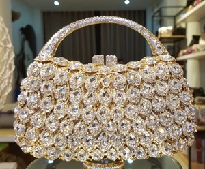 Detail of gold metal evening clutch bag featuring teardrop crystals and round handle