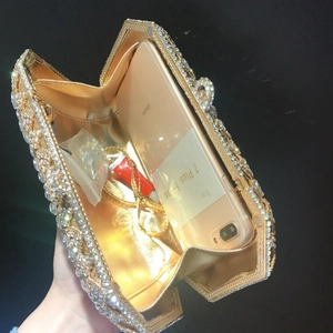 Detail view of gold evening clutch interior holding a large smartphone and cosmetics