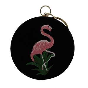 Detailopname van flamingo-borduurwerk en groene bladmotieven op een zwarte ronde avondtas