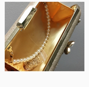 Détail d'une pochette de soirée avec anse en perles, chaîne dorée et extérieur champagne