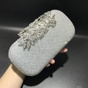 Silver evening clutch with rhinestones and leaf motif held in hand against black backdrop