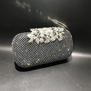 Detailed macro view of the crystal encrusted floral clasp on the black evening clutch bag