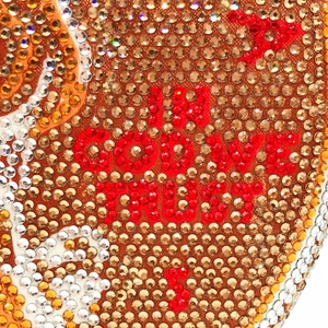 Macro shot of In God We Trust red rhinestone lettering on a luxury evening clutch bag