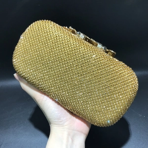 Close-up of a hand holding a gold crystal clutch bag with leaf-patterned rhinestones