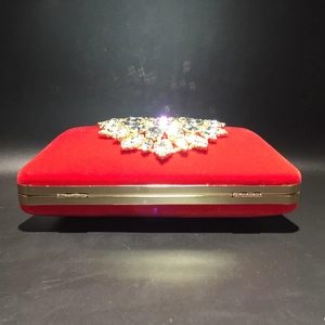 Detail of red velvet evening clutch featuring crystal floral clasp and gold metal frame