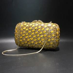 Macro shot of gold evening clutch featuring yellow crystals and a fine metal chain strap
