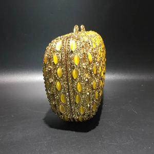 Detailed side view of luxury evening clutch with gold metal frame and yellow stones