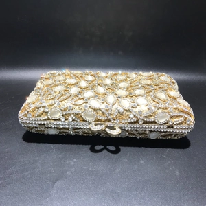 Detailed close-up of golden hollow metal clutch bag with white cat-eye stones and rhinestones