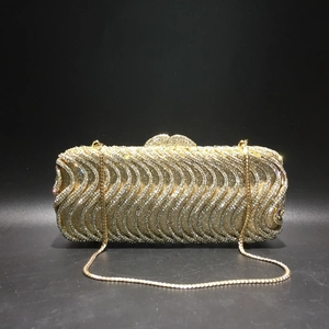 Detail of gold evening clutch bag with S-shaped wavy rhinestones and metal chain strap