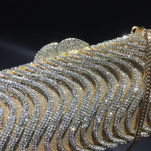 Macro detail of wave-patterned gold clutch bag with dense sparkling crystals and metal chain