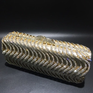 Macro view of gold evening clutch bag with S-shaped rhinestone patterns and crystal clasp