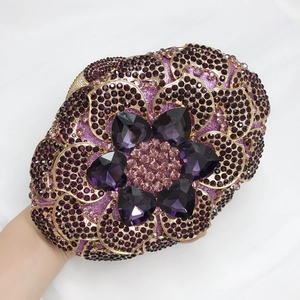 Detail of luxury purple floral clutch bag with heart crystals and gold trim held by hand