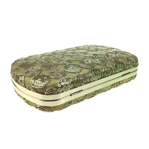 Macro view of golden sequin lace clutch with metallic frame and swirl embroidery texture