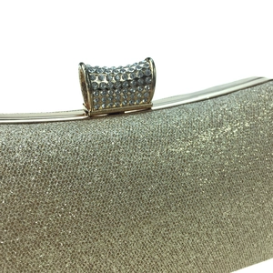 Close-up of golden evening clutch featuring sparkling glitter finish and rhinestone clasp