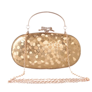 Detail of golden oval evening clutch bag with textured surface and rhinestone bow clasp