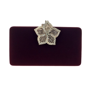 Détail d'une pochette en velours bordeaux avec fermoir fleur dorée et strass brillants