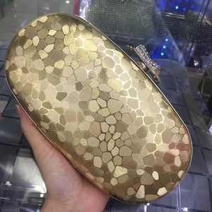 Detail of gold oval clutch with geometric texture and rhinestone bow clasp for evening