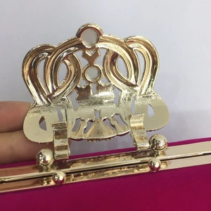 Close-up of rose red velvet evening bag featuring a polished gold crown-shaped clasp