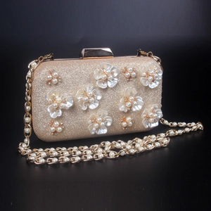 Détail d'une pochette champagne avec fleurs de perles 3D et bandoulière en chaîne