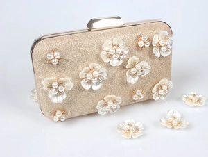 Détail de pochette de soirée or champagne avec fleurs blanches et perles au centre