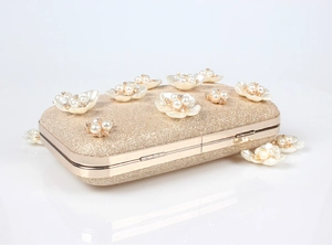 Détail de pochette de soirée avec fleurs 3D et perles sur tissu pailleté doré
