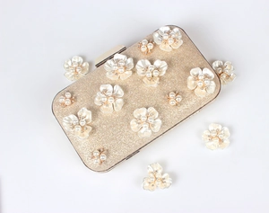 Détail d'un sac de soirée pailleté doré avec fleurs 3D en perles et fermoir métal