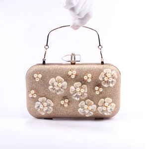 Close-up of golden evening clutch with white pearl flowers and crystal clasp detail