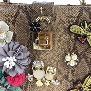 Détail du sac à main motif serpent avec fleurs 3D et breloques de hibou en strass