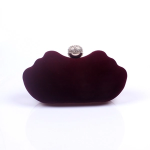Close-up of burgundy velvet evening clutch with wavy edges and rhinestone sphere clasp