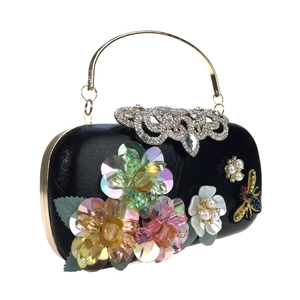 Detail view of 3D sequin flowers, pearl petals, and rhinestone bee on black evening clutch
