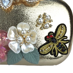 Macro shot of gold evening clutch featuring 3D floral petals, pearl bee, and beadwork