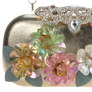 Close-up of golden evening clutch featuring crystal flowers, pearls and green leaves