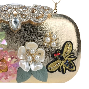 Detail of gold evening clutch with crown crystal clasp and 3D floral bee embroidery