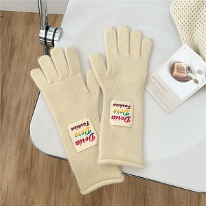 Close-up of beige knit gloves with a colorful fashion woven label on a minimal chair
