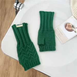 Close-up of dark green cable knit fingerless gloves with a branded fabric label