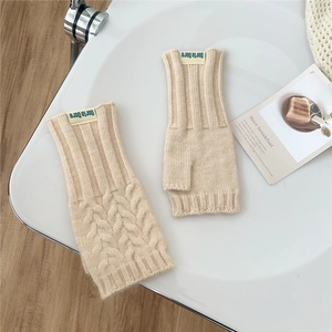 Close-up of beige cable knit fingerless gloves with Doria Dore brand label on a table