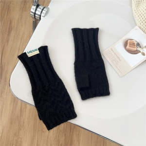 Detail of black cable-knit fingerless gloves with a small fabric brand label on a table