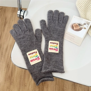 Detail of grey knitted gloves featuring a colorful Doria Dore fashion alphabet patch