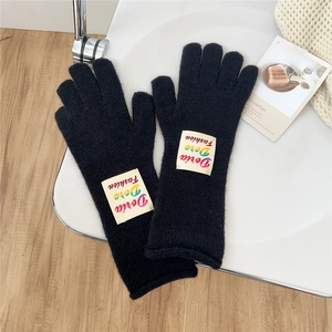 Detail of black knitted gloves with elongated cuffs and colorful logo tag on soft fabric