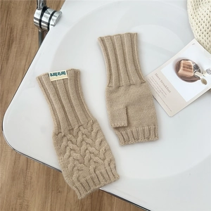 Detailed cable knit pattern on beige fingerless gloves with a small brand label