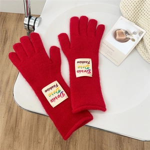 Close-up of soft red knitted gloves with a fashion patch on cozy home background